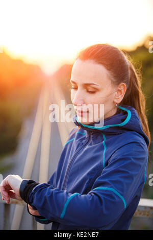 Portrait of young sporty woman checking heart rate on fitness watch. Athletic girl standing outdoor after fitness training Stock Photo
