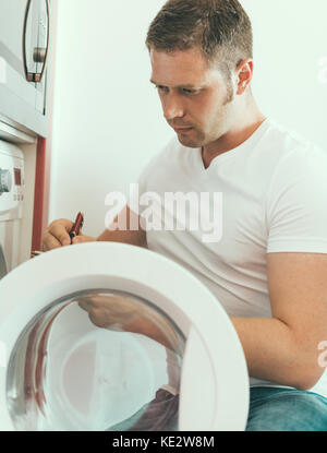 Male technician repairing washing machine, writing the manufacturer's code. Stock Photo