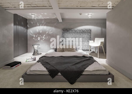 Gray and white bedroom with floor bed and brick ceiling Stock Photo