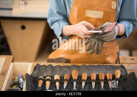 Young female woodworker using smartphone at work Stock Photo