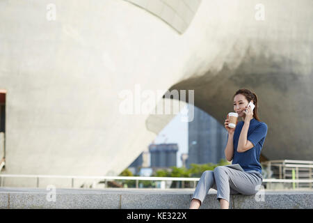 Young smiling businesswoman talking on cellphone drinking takeout coffee Stock Photo