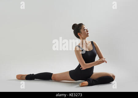 Side view of young ballerina in black leotard posing stretching Stock Photo