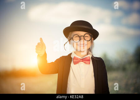Funny little girl in bow tie and bowler hat showing thumb up. Stock Photo