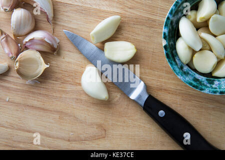Peeled garlic cloves on cutting board with knife and bowl fro from directly above. Stock Photo