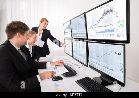 Happy Young Stock Market Brokers Looking At Graphs On Multiple Computer In Office Stock Photo