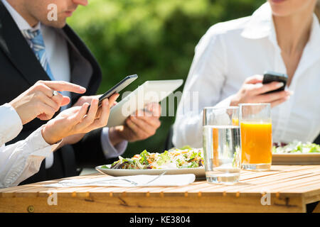 Businesspeople Using Mobile Phone With Food And Glass Of Juice On Table Stock Photo