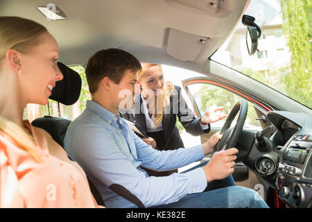 Young Happy Female Saleswoman Showing New Car To Couple Stock Photo