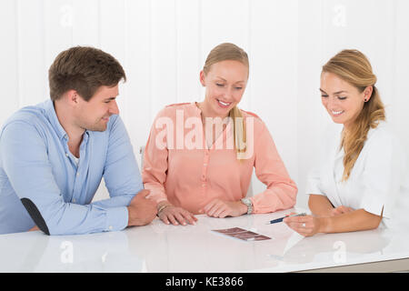 Happy Female Doctor Showing Ultrasound Scan To Young Couple In Clinic Stock Photo