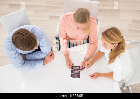 High Angle View Of Female Doctor Showing Ultrasound Scan To Young Couple In Clinic Stock Photo