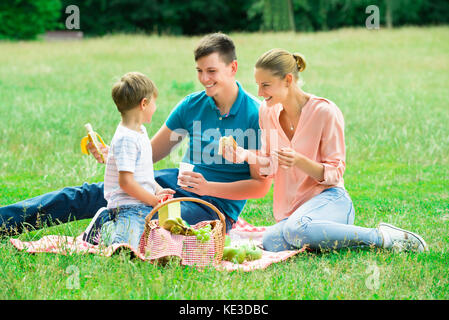 Young Happy Family Enjoying Breakfast At Picnic In The Park Stock Photo