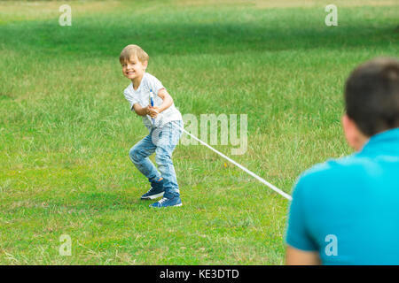 Happy Kid Pulling A Rope In Tug Of War At The Park With His Father Stock Photo