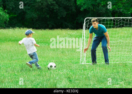 Father And Son Playing Soccer On A Green Grass In The Park Stock Photo