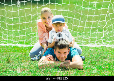 Happy Family With Soccer Ball Lying  In Front Of The Soccer Net Stock Photo