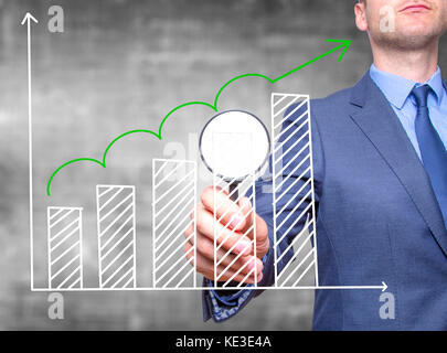 Sales Growth Graph - Business man holding magnifying glass on screen interface Stock Photo