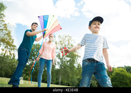 Happy Family Enjoying Playing With The Colorful Kite In The Park Stock Photo