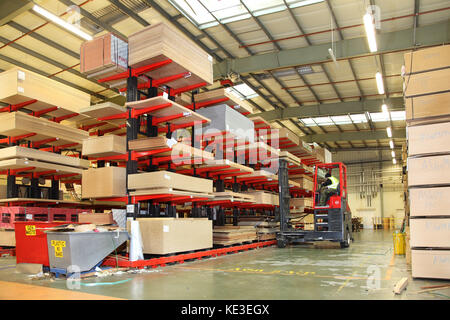 A fork lift truck removes timber sheet products stacked in a modern, UK distribution warehouse. Stock Photo