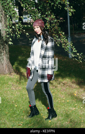 Young beautiful stylish woman, wearing a coat in a white and black cage, white jacket, gray trousers, black boots. Street style, spring and autumn trend, a flirty look Stock Photo