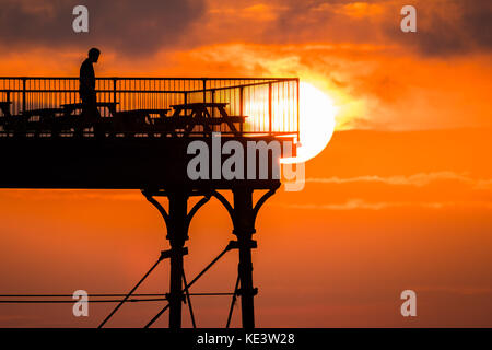 Aberystwyth Wales UK, Wednesday 18 October 2017 UK Weather: In a period of calm conditions between Storm Ophelia and the incoming Storm Brian (scheduled for Saturday), people enjoy the last moments of the setting sun over the seaside Royal Pier in Aberystwyth on the Cardigan Bay coast of west wales Photo Credit: Keith Morris/Alamy Live News Stock Photo