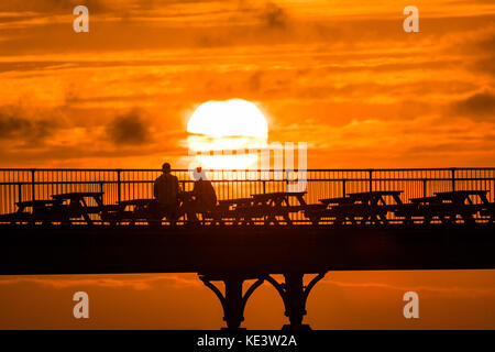 Aberystwyth Wales UK, Wednesday 18 October 2017 UK Weather: In a period of calm conditions between Storm Ophelia and the incoming Storm Brian (scheduled for Saturday), people enjoy the last moments of the setting sun over the seaside Royal Pier in Aberystwyth on the Cardigan Bay coast of west wales Photo Credit: Keith Morris/Alamy Live News Stock Photo