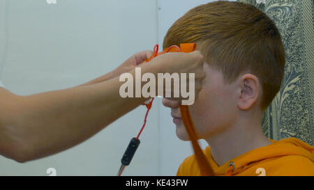 European child conduct electroencephalography. A process fragment. Rheoencephalography - a doctor attaches electrodes on a patients head Stock Photo