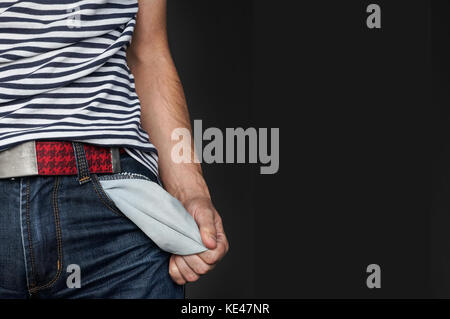 Young man pulling out empty pocket on black isolated background. A guy without money, with empty pockets. Left place for text Stock Photo