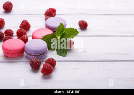 Closeup view of macaroons with raspberries with mint over white wooden background. Place or space for text Stock Photo
