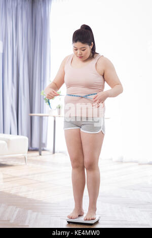 Young fat woman measuring her waist standing on a scale Stock Photo