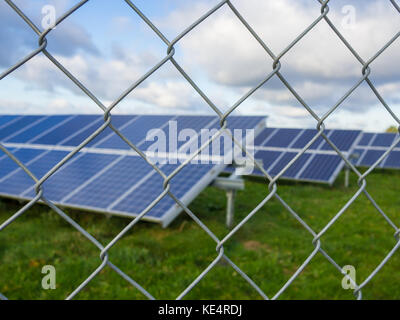 Solar panel or photovoltaic farm behind metal fence on green field with dramatic cloudy sky in North Germany. Stock Photo