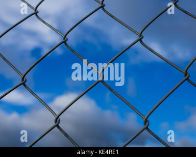 Closeup of metal fence with square units in front of dramatic blue cloudy sky. Stock Photo