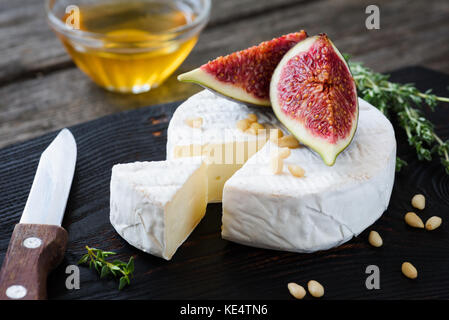 Camembert cheese with figs, honey and pine nuts on dark wooden cutting board. Closeup view Stock Photo