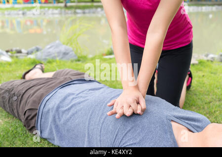 Woman giving cardiopulmonary resuscitation (CPR) to a man at public park Stock Photo