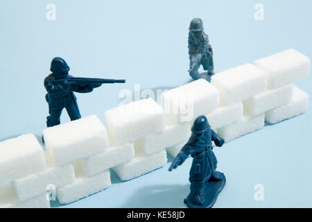 Battlefield with plastic soldiers separated by a wall border of white sugar cubes. Minimal color still life photography Stock Photo