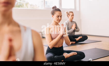 Young woman in yoga class doing meditation lotus pose. Group of healthy people meditating in a yoga studio. Stock Photo