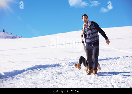 Young playful couple having fun sledging down snow covered hill Stock Photo