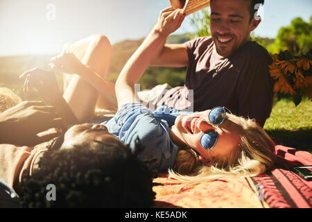 Playful young friends laughing, relaxing on picnic blanket in sunny summer park Stock Photo