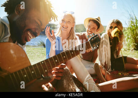 Young friends laughing and playing guitar, enjoying sunny summer picnic Stock Photo