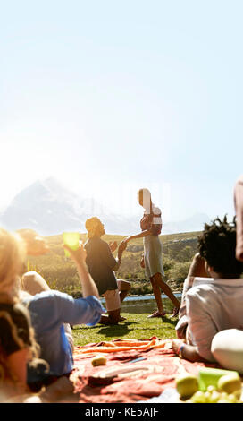 Friends watching young man proposing to woman at sunny summer picnic Stock Photo