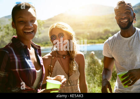 Portrait enthusiastic young friends drinking at sunny summer riverside Stock Photo