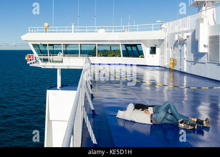 Young couple in love laying embraced in sunshine on deck of Stena Line ferry between Sweden and Denmark  Model Release: No.  Property Release: No. Stock Photo