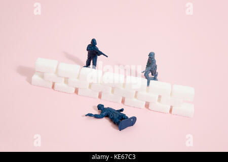 Battlefield with plastic soldiers separated by a wall border of white sugar cubes. Minimal color still life photography Stock Photo