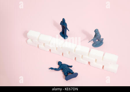 Battlefield with plastic soldiers separated by a wall border of white sugar cubes. Minimal color still life photography Stock Photo