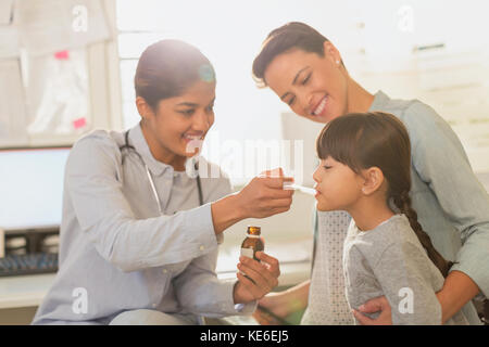 Female pediatrician feeding cough syrup to girl patient in examination room Stock Photo