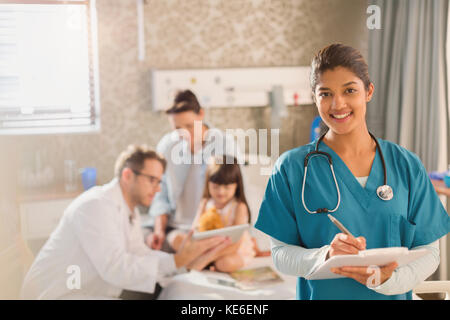 Portrait confident female nurse taking notes on medical record while doctor shows digital tablet to girl patient in hospital Stock Photo