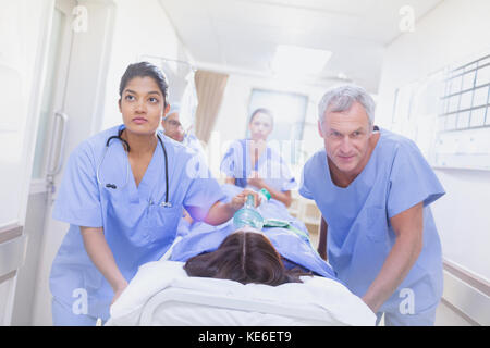 Determined surgeons pushing female patient on stretcher down hospital corridor Stock Photo