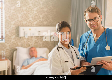 Portrait smiling, confident doctor and nurse making rounds, using digital tablet and clipboard in hospital room Stock Photo