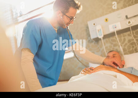 Male nurse using stethoscope on patient in hospital bed Stock Photo