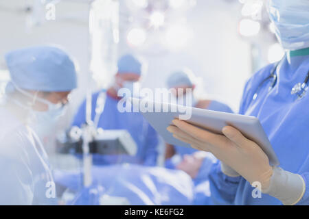 Surgeon wearing rubber gloves, using digital tablet in operating room Stock Photo