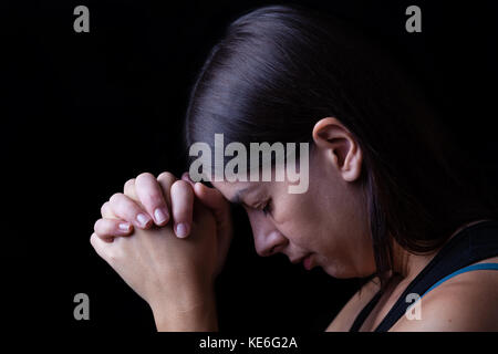 Faithful woman praying, hands folded in worship to god, head down, eyes closed in religious fervor. black background prayer faithful hands folded Stock Photo