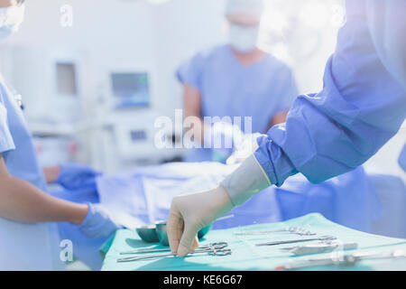 Surgeon in rubber gloves reaching for surgical scissors on tray in operating room Stock Photo