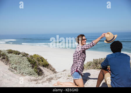 Woman placing hat on boyfriend on sunny summer ocean beach Stock Photo